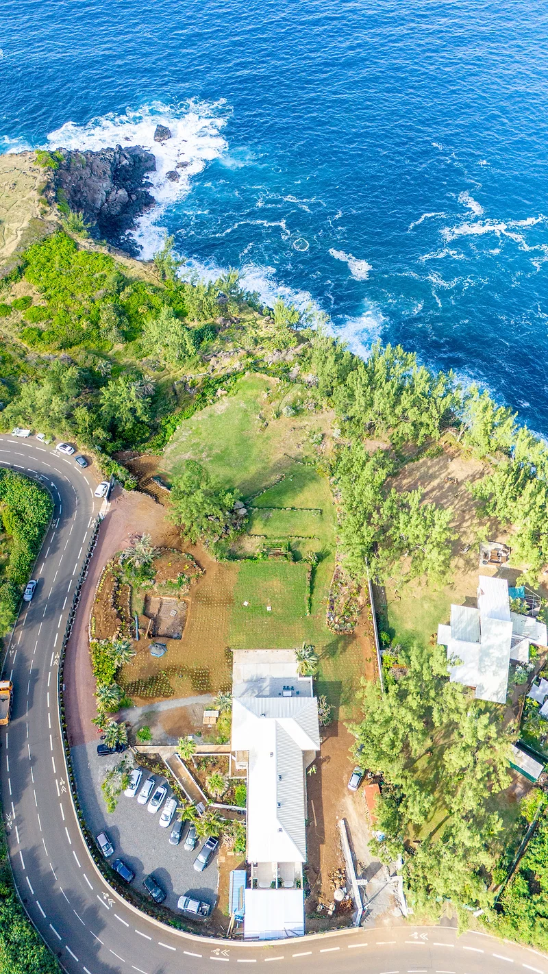 Le domaine vu d'en haut : la route et le parking, les bâtiments, le jardin en terrasses, puis la falaise et l'océan